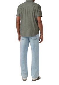 Olijfgroene overhemd met korte mouwen en een omgevouwen kraag, voorzien van witte stiksels. Gecombineerd met lichtblauwe wijdvallende jeans en casual schoenen.