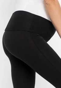 Leggings noirs avec une taille haute, fabriqués en matériau élastique. Texture lisse avec des coutures le long des jambes, silhouette ajustée.