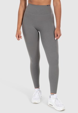 Leggings grigi alti in vita realizzati in un tessuto elastico e liscio con un design senza cuciture. Indossati con sneakers da atleta bianche.