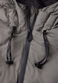 Chaqueta gris acolchada con collar alto, cremallera frontal y cordones ajustables con marca. El tejido texturizado contrasta con secciones lisas.