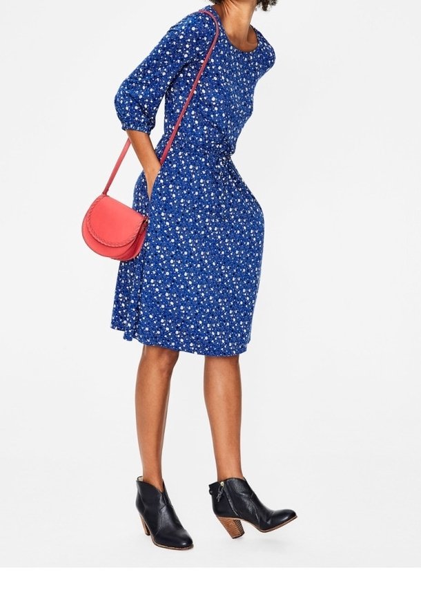 Blå blomsterklänning med trekvartsärmar, som har en figurnära midja och en svängande kjol. I kombination med en röd axelväska och svarta ankelstövlar.