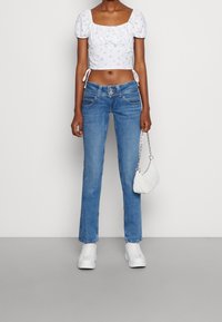 Vit croppad topp med puffärmar och blommönster, tillsammans med ljusblå raka jeans, vita sneakers och en liten vit väska.