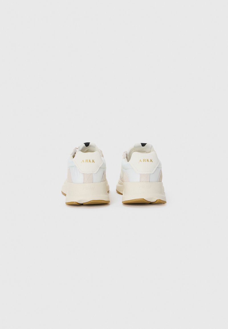 Weiße und beige Sneakers mit einem strukturierten Design, ausgestattet mit einer gepolsterten Sohle und einem schwarzen Akzent an der Ferse. Goldene Markenbildung an der Rückseite.