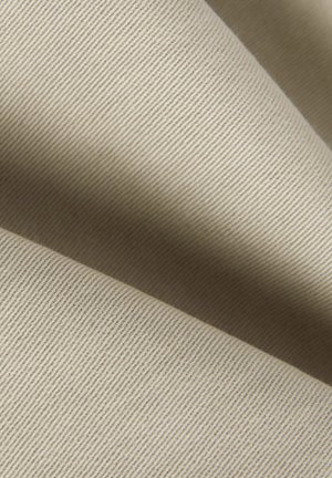 Beige tyg med en fin ribbad struktur, som visar en slät yta och en subtil glans, draperad i mjuka veck.