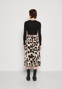 Top corto negro de manga larga combinado con una falda de leopardo hasta la rodilla. Modelo que lleva botas negras hasta el tobillo, con textura suave y tela blanda.