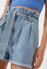 Lichtblauwe denim short met een hoge, gerimpelde tailleband en bijpassende strikriem. Kenmerkt plooien en opgerolde zoomranden. Soepele textuur overal.