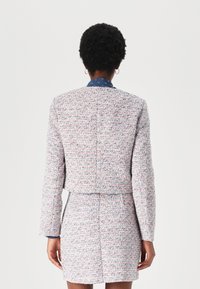 Veste en tweed texturé et multicolore avec un design court. Dotée de manches longues et d'un col bleu marine, accompagnée d'une jupe assortie.