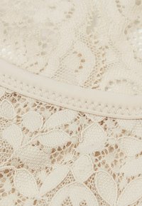 Tejido de encaje beige con patrones florales y una banda elástica suave en la parte superior, que muestra un detalle y textura intrincados.