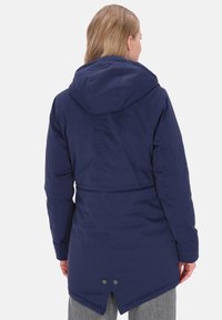 Granatowa parka z kapturem, regulowanym pasem i dwoma guzikami z tyłu. Gładka, teksturowana tkanina, z dłuższym tylnym dołem dla lepszej ochrony.