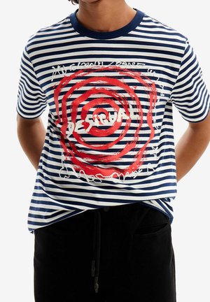 Osoba ubrana w granatowo-biały pasiasty t-shirt z czerwonym spiralnym wzorem i napisem "Desigual", w połączeniu z czarnymi spodniami.