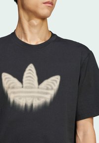 Sort bomulds T-shirt med et fremtrædende, falmet hvidt tre-blads logo design. Rund hals og korte ærmer. Glat tekstur.