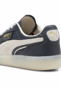 Puma Palermo sportbačiai turi tamsiai mėlyną odinį paviršių, smėlio spalvos zomšos akcentus, perforuotą dizainą, auksinį logotipą ir pusiau skaidrų gumos padą.