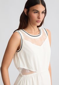 Abito bianco senza maniche con un top in rete con bordo nero, scollatura a V e tessuto arricciato in vita con dettagli a taglio.