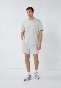 Light grey cotton t-shirt with short sleeves paired with matching shorts. Features a relaxed fit and smooth texture. Worn with athletic shoes.