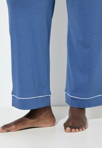 Blaue Baumwoll-Loungehosen mit geradem Schnitt, mit weißen Nähten am Saum. Füße sichtbar in einem natürlichen Hautton.