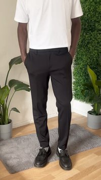 Calças pretas sob medida com um acabamento suave, apresentando bolsos frontais e um corte slim. Combinadas com sapatos pretos e uma t-shirt branca.
