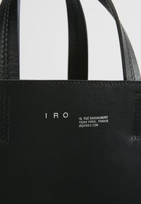 Black leather tote bag with two sturdy handles. Features embossed branding and detail on one side. Smooth texture with visible stitching.