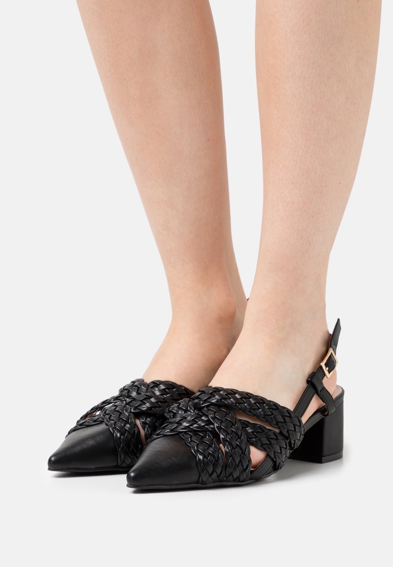 Des chaussures à talons noirs présentent des détails tissés à l'avant, un bout pointu et un petit talon carré, avec une bride à la cheville et une boucle ajustable.