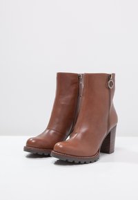 Bottines en cuir marron avec une fermeture éclair sur le côté, semelle en caoutchouc texturé et talon empilé. Fini lisse et détail en métal circulaire.