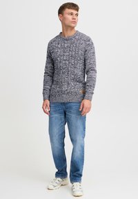 Gray and white textured knit sweater with crew neckline, paired with light blue jeans and white sneakers. Features a leather brand patch on the sweater.