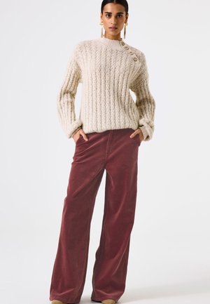 Creme gebreide trui met ribbelstructuur en een zijknopdetail, gecombineerd met wijde bordeauxkleurige corduroy broek. Glad textuur, casual ontwerp.