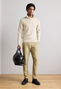 Μπεζ ριγωτό πουλόβερ με γιακά μισού φερμουάρ, ανοιχτό κίτρινο παντελόνι και υφασμένη μαύρη τσάντα. Μαύρα μοκασίνια ολοκληρώνουν την εμφάνιση.