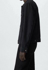 Giacca di jeans nera con un design aderente, dettagli con bottoni e tasche frontali. Tessuto liscio, maniche lunghe e collo a camicia.