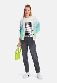 Knit cardigan in light blue, green, and cream, striped shirt, gray jeans, and white sneakers with neon green accents, paired with a small neon bag.