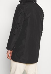 Veste noire matelassée avec un col haut et des manches longues. Présente un design élégant et des détails cousus le long des côtés.