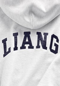 Szara bluza z kapturem w kolorze wrzosu z dużym granatowym napisem "LIANG" na plecach. Miękki, teksturowany materiał z kapturem i swobodnym, luźnym krojem.