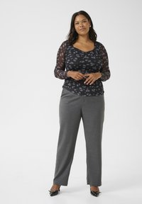 Haut floral noir à manches longues avec des manches transparentes, associé à un pantalon gris ajusté et des escarpins noirs à bout pointu. Design simple et élégant.