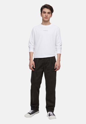 White long-sleeve shirt with small black text, paired with black loose-fit pants and black sneakers with white accents.