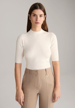 Haut en maille côtelée beige clair avec un col haut et des manches courtes, associé à un pantalon tailleur taupe doté d'un bouton et de quincaillerie décorative.