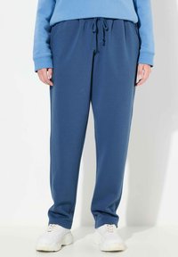 Niebieskie dresy wykonane z miękkiego materiału, z elastycznym pasem ze sznurkiem, bocznymi kieszeniami i luźnym krojem. Stylizowane z białymi trampkami.