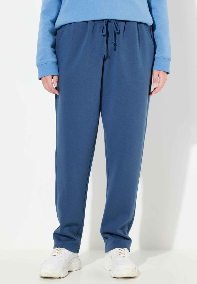 Niebieskie dresy wykonane z miękkiego materiału, z elastycznym pasem ze sznurkiem, bocznymi kieszeniami i luźnym krojem. Stylizowane z białymi trampkami.