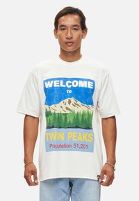 Witte katoenen T-shirt met een grafische print van bergen, bomen en "Welkom in Twin Peaks" in blauw en geel. Korte mouwen, relaxed fit.