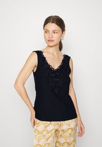 Top preto sem mangas com decote em V, apresentando um intrincado bordado floral na gola. Tecido suave com uma textura lisa.