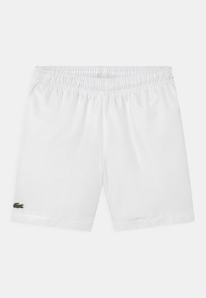 Pantalones cortos blancos con cinturilla elástica y un pequeño logo verde de cocodrilo en la parte inferior de la pierna izquierda, mostrados sobre un fondo sencillo.