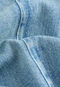 Világoskék farmeranyag lágy tapintással, látható varrási vonalakkal és klasszikus átlós szövésmintával.