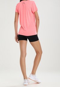 Kirkkaan vaaleanpunainen lyhythihainen rento t-paita, yhdistettynä mustiin urheilushortseihin ja valkoisiin lenkkareihin, esitetty takaa.