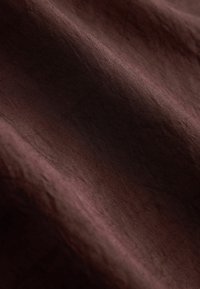 Gros plan d'un tissu brun foncé froissé montrant une texture fine et des reflets lumineux subtils.