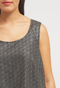 Bezramenný top z černé látky se stříbrnými skvrnami, s kulatým výstřihem a měkkou texturou, střižený pro volný střih.