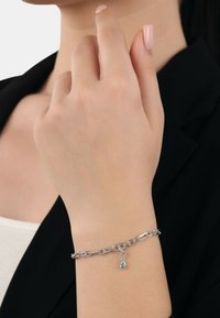 Bracciale in argento con maglie allungate e un piccolo charm blu a forma di goccia. Texture liscia con finitura lucida.