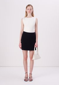 Haut blanc à côtes, jupe plissée noire, sandales noires à lanières et petit sac à main blanc. Les vêtements présentent des lignes épurées et des couleurs contrastées.