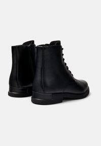 Botas negras de piel hasta el tobillo con un acabado suave, con cordones en la parte delantera y detalle de cremallera en el lateral. Tacón cuadrado, puntera redondeada y diseño minimalista.
