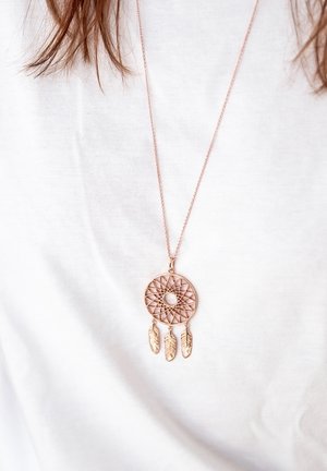 Collier avec pendentif attrape-rêves en or rose, présentant un design de maillage circulaire et trois accents de plumes. La chaîne est délicate et simple.