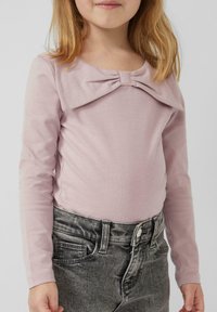 Hellrosa Langarmoberteil mit großer Schleifendetail am Ausschnitt, kombiniert mit grauen Jeans mit Knopf und Taschen.