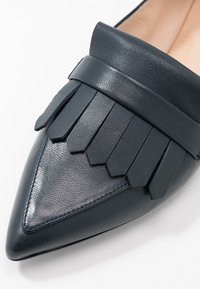 Mocassins en cuir bleu marine à bout pointu avec une finition texturée, dotés d'une large lanière et d'un détail de franges superposées sur l'empeigne. Doublure intérieure lisse.