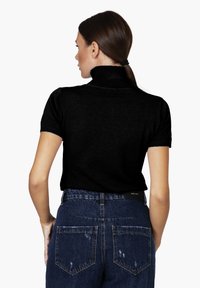Schwarzer Turtleneck-Pullover mit kurzen Ärmeln, ribbeltem Kragen und taillierter Passform, kombiniert mit hoch geschnittenen blauen Jeans aus Denim mit distressierten Akzenten.