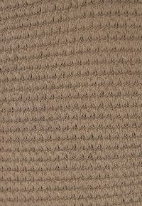 Beige színű, texturált anyag, amely kis kiemelkedő hurkokból álló szőtt mintát mutat, egyenletes, enyhén rugalmas felületet kialakítva. Könnyű és lélegző.